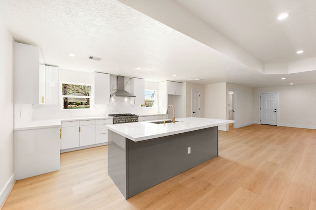 kitchen featuring visible vents, stove, white cabinets, a sink, and wall chimney exhaust hood