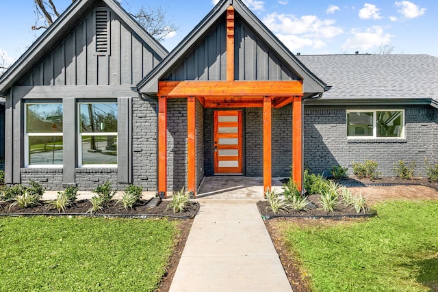 view of front facade with board and batten siding, a front yard, brick siding, and a shingled roof