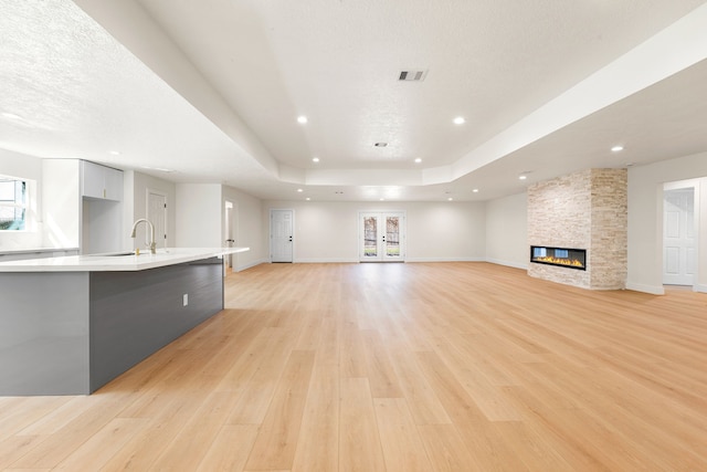 unfurnished living room featuring a sink, a fireplace, light wood-type flooring, and a raised ceiling