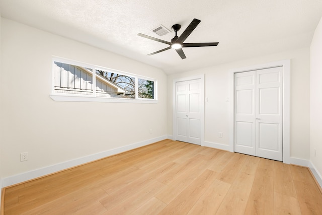 unfurnished bedroom featuring baseboards, visible vents, wood finished floors, a textured ceiling, and multiple closets