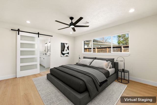 bedroom featuring wood finished floors, visible vents, baseboards, and a barn door