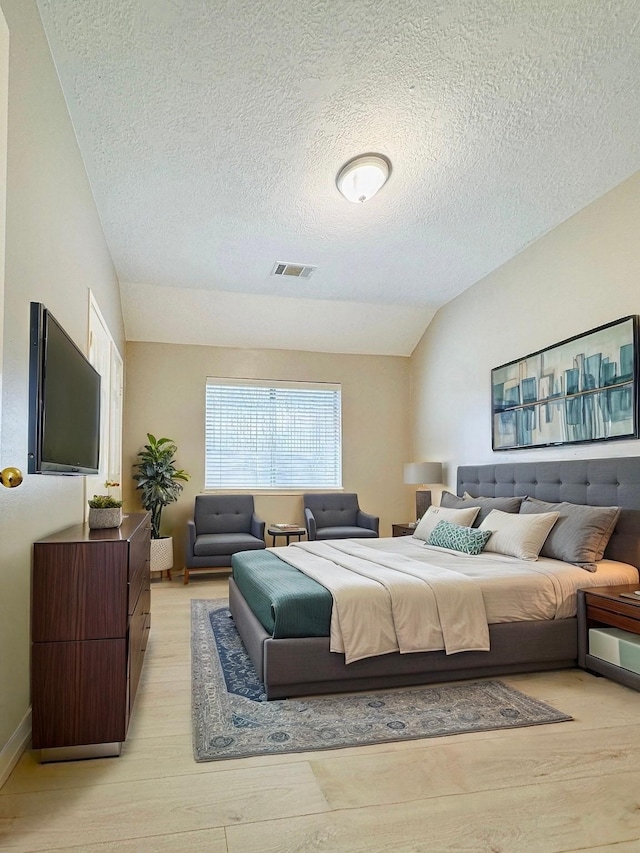 bedroom featuring lofted ceiling, visible vents, a textured ceiling, and light wood-style flooring