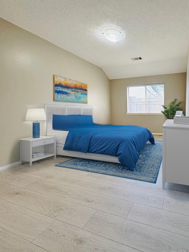 bedroom with a textured ceiling, vaulted ceiling, visible vents, and baseboards