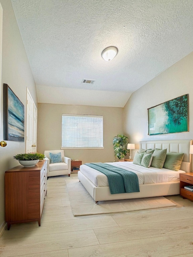 bedroom featuring lofted ceiling, light wood-type flooring, visible vents, and a textured ceiling