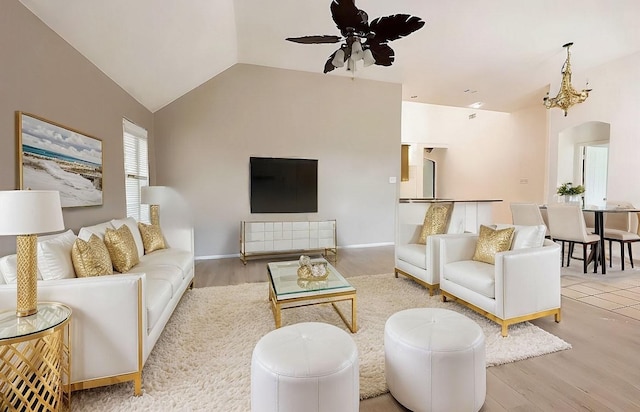 living area with arched walkways, lofted ceiling, wood finished floors, baseboards, and ceiling fan with notable chandelier