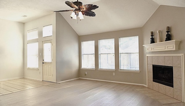 unfurnished living room featuring light wood-style floors, lofted ceiling, a wealth of natural light, and a tiled fireplace