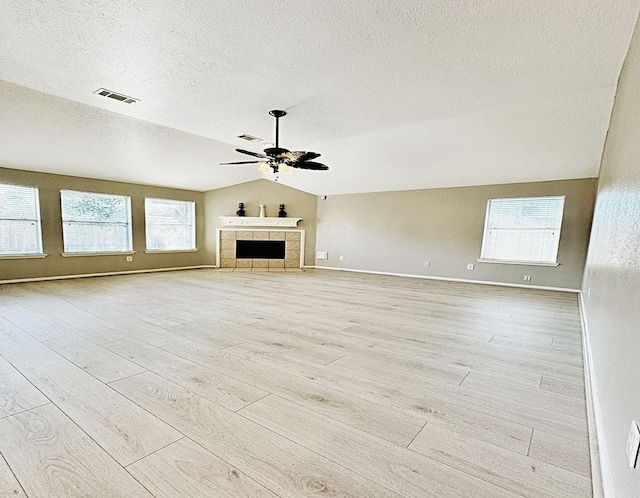 unfurnished living room featuring light wood finished floors, visible vents, a tiled fireplace, a ceiling fan, and vaulted ceiling