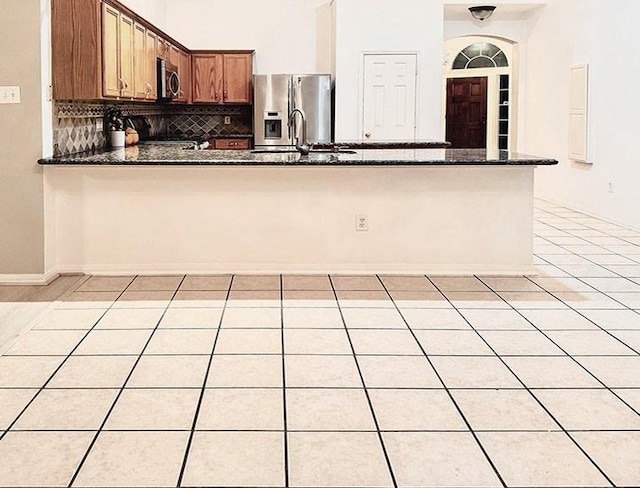 kitchen with brown cabinets, backsplash, appliances with stainless steel finishes, dark stone countertops, and a peninsula