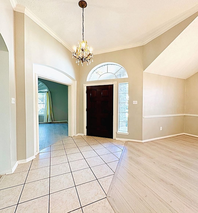 entrance foyer with a notable chandelier, baseboards, vaulted ceiling, light wood-type flooring, and crown molding