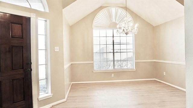 foyer entrance featuring lofted ceiling, baseboards, wood finished floors, and an inviting chandelier