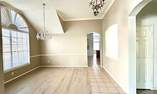 unfurnished dining area with arched walkways, ornamental molding, a textured ceiling, light wood-type flooring, and a chandelier