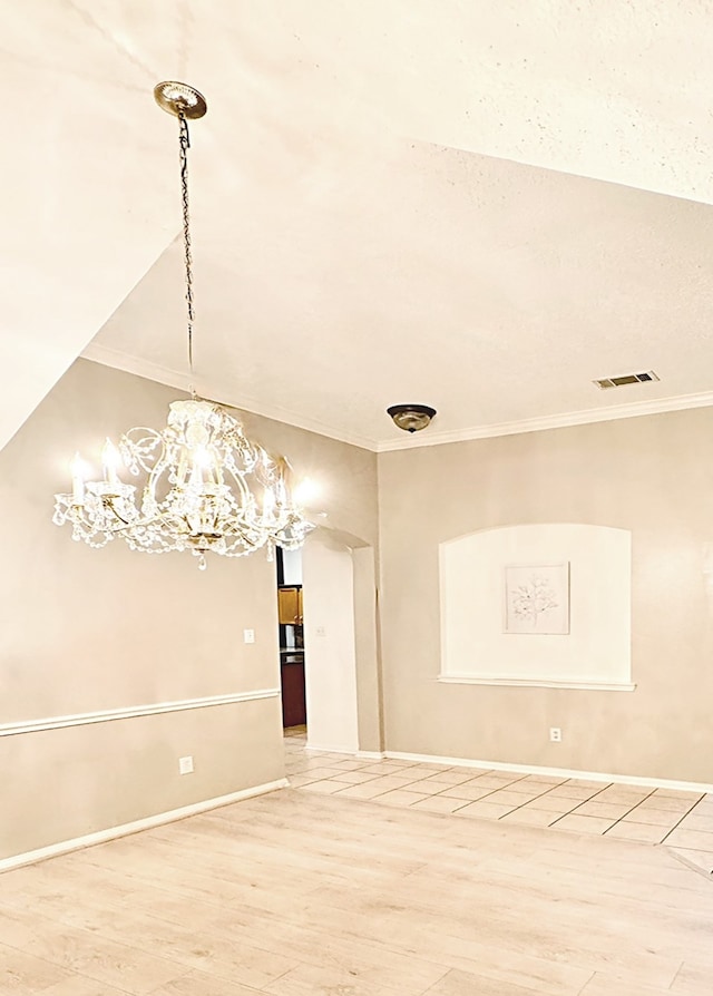 empty room with a notable chandelier, visible vents, ornamental molding, wood finished floors, and baseboards