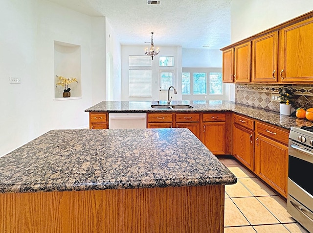 kitchen featuring tasteful backsplash, brown cabinetry, white dishwasher, a sink, and a peninsula