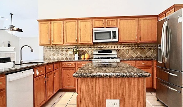 kitchen with light tile patterned floors, white appliances, dark stone countertops, and a sink