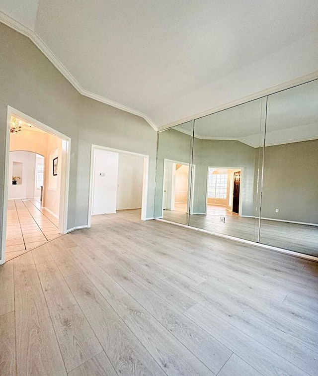 unfurnished bedroom with arched walkways, crown molding, a closet, ensuite bath, and wood finished floors