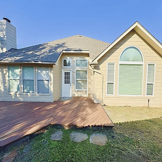 rear view of property featuring a shingled roof, a chimney, and a wooden deck