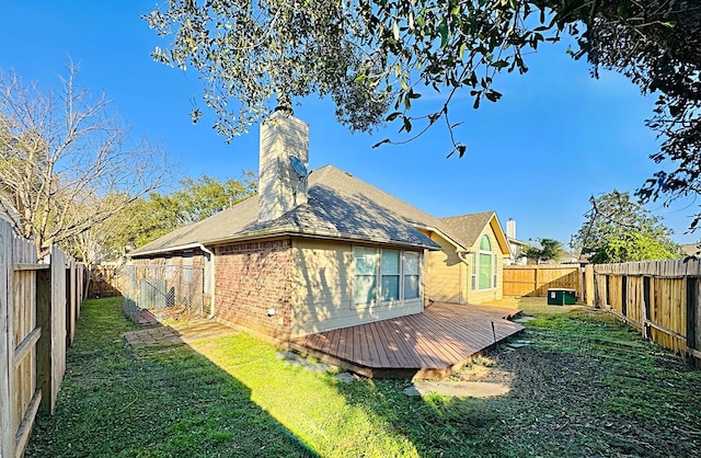 back of house with brick siding, a chimney, a lawn, a fenced backyard, and a wooden deck