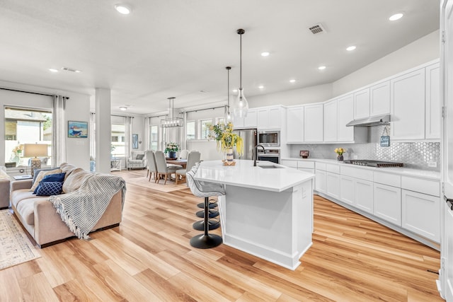 kitchen with stainless steel appliances, visible vents, light wood-style floors, open floor plan, and tasteful backsplash