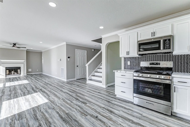 kitchen with stainless steel appliances, a glass covered fireplace, light countertops, and white cabinets