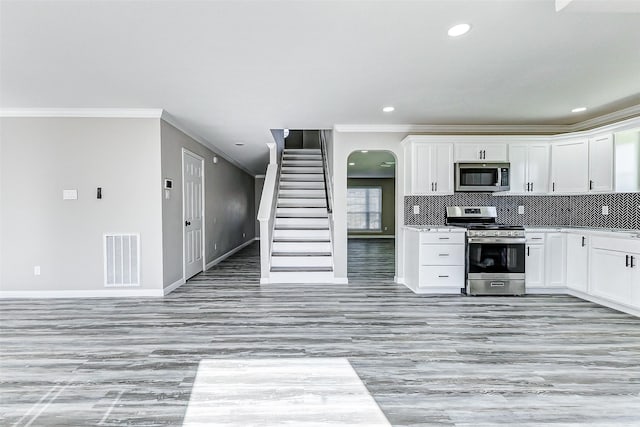 kitchen featuring arched walkways, stainless steel appliances, visible vents, white cabinets, and decorative backsplash