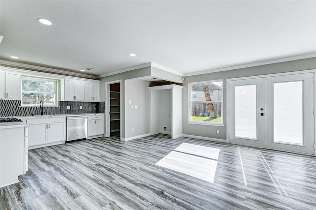 kitchen with light wood finished floors, tasteful backsplash, stainless steel dishwasher, white cabinetry, and baseboards