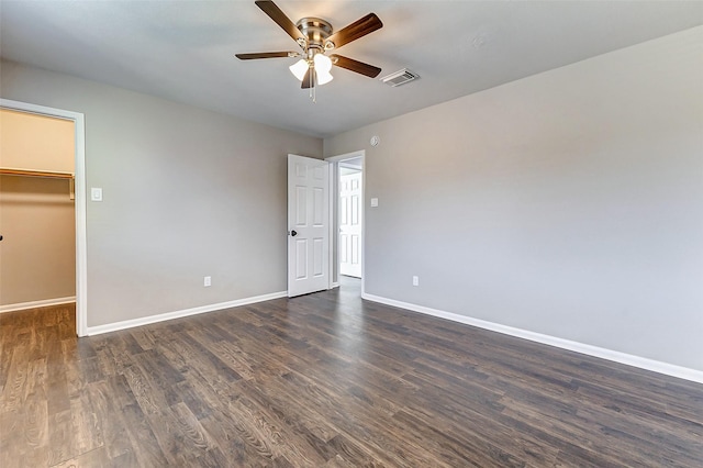 unfurnished bedroom featuring dark wood-style floors, a walk in closet, visible vents, ceiling fan, and baseboards