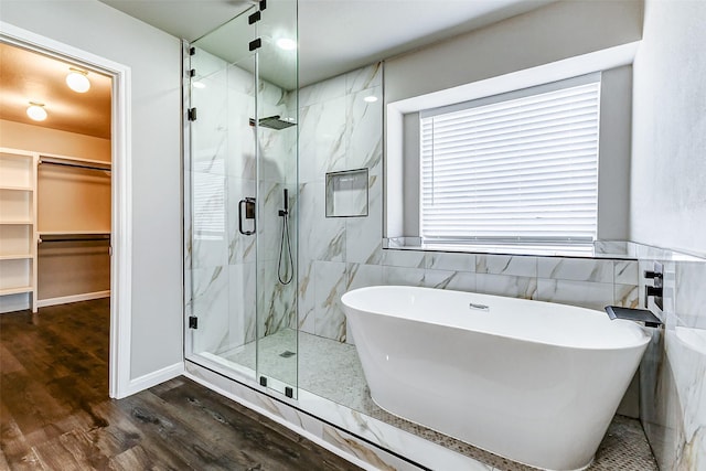 full bath with a marble finish shower, a soaking tub, wood finished floors, a spacious closet, and tile walls