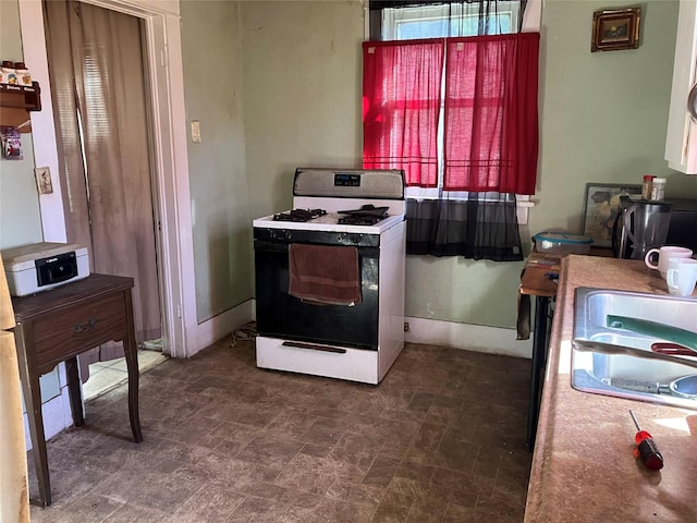 kitchen with gas stove, a sink, and baseboards