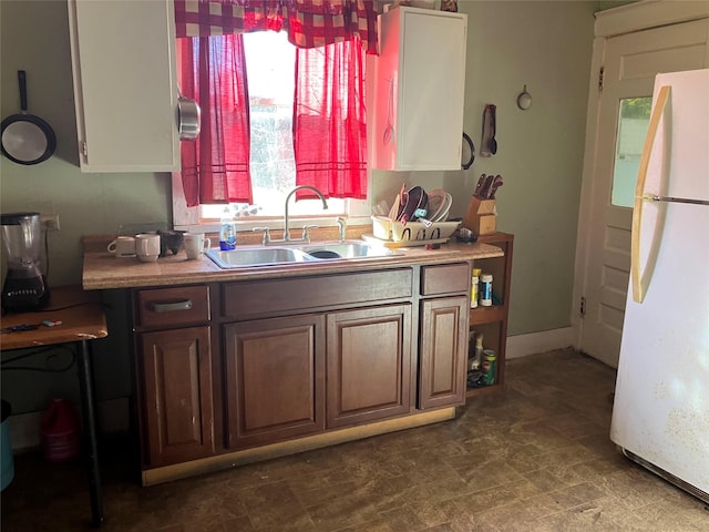 kitchen featuring freestanding refrigerator, light countertops, a sink, and baseboards