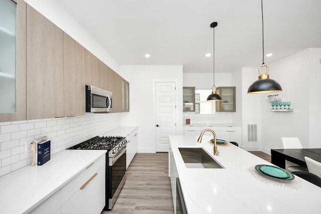 kitchen featuring gas range, modern cabinets, stainless steel microwave, light wood-style floors, and a sink