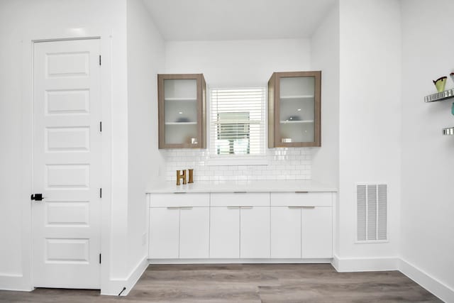 kitchen featuring tasteful backsplash, light countertops, visible vents, and glass insert cabinets