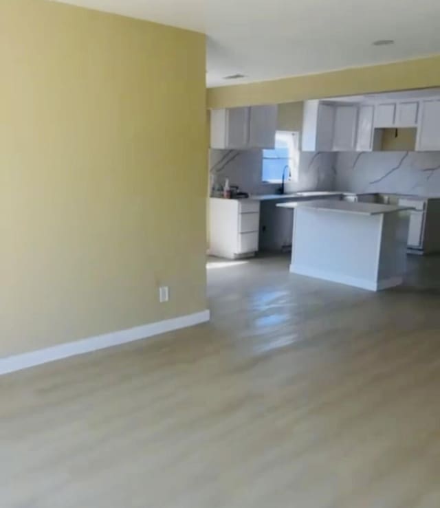 kitchen with baseboards, white cabinets, a kitchen island, light wood-style floors, and backsplash