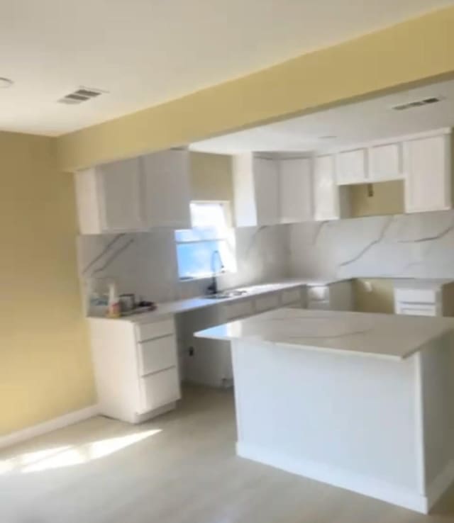 kitchen featuring a sink, a kitchen island, visible vents, white cabinetry, and tasteful backsplash