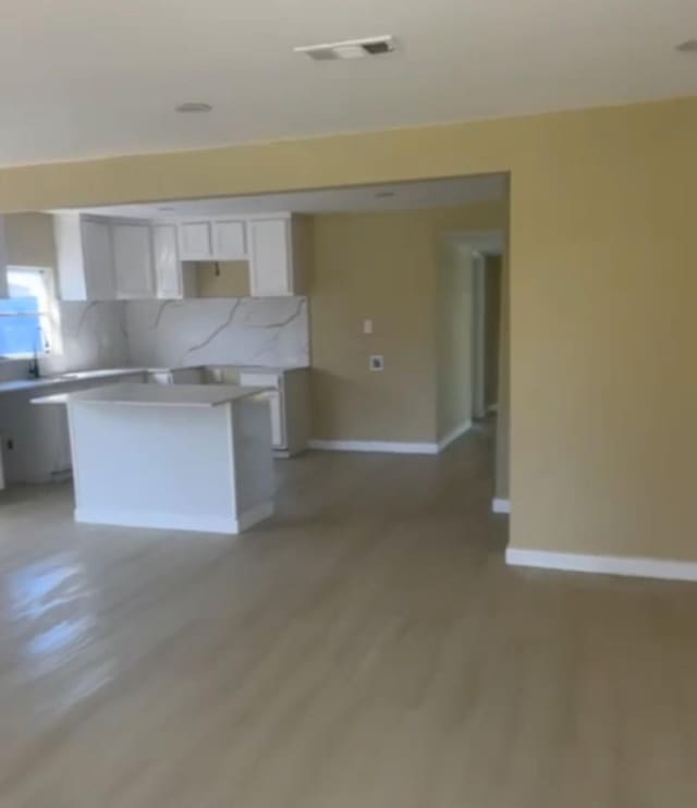 kitchen featuring light wood-style flooring, a kitchen island, visible vents, baseboards, and white cabinets