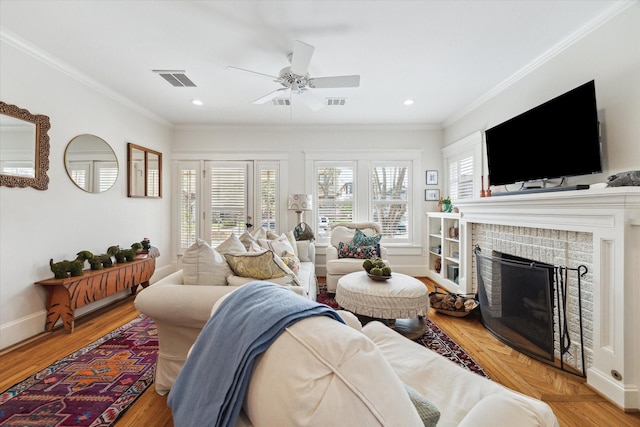 living room with crown molding, visible vents, a brick fireplace, wood finished floors, and baseboards