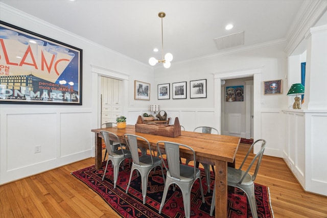 dining space featuring light wood-style floors, visible vents, ornamental molding, and a decorative wall