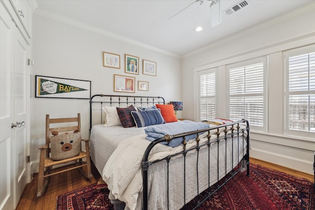 bedroom with ornamental molding, multiple windows, wood finished floors, and visible vents