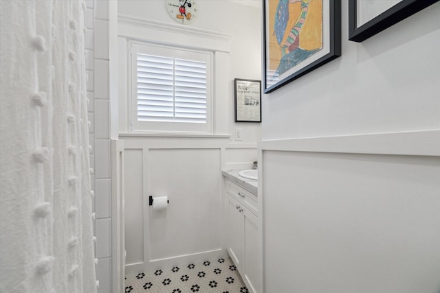 bathroom with a shower, wainscoting, a decorative wall, and vanity