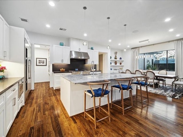 kitchen featuring under cabinet range hood, a breakfast bar, a sink, white cabinets, and dark wood-style floors