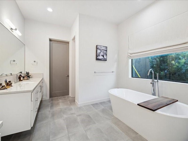 bathroom with a freestanding bath, recessed lighting, vanity, and baseboards