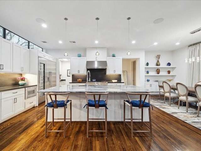 kitchen with under cabinet range hood, visible vents, dark wood-style flooring, and built in fridge