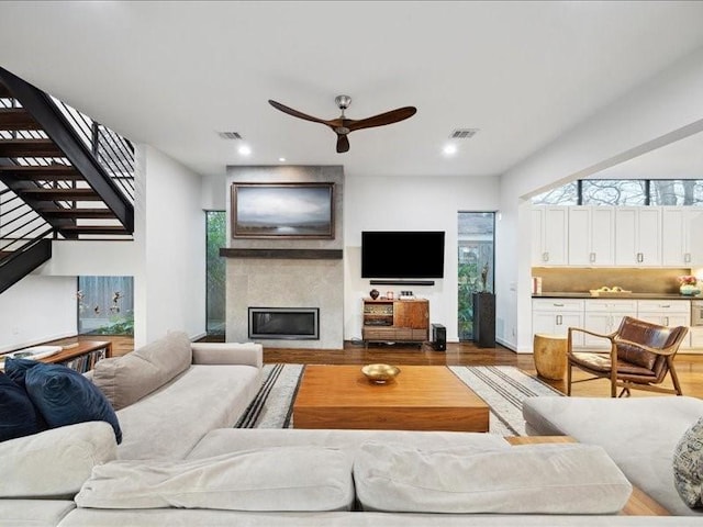 living room featuring a large fireplace, stairs, wood finished floors, and visible vents