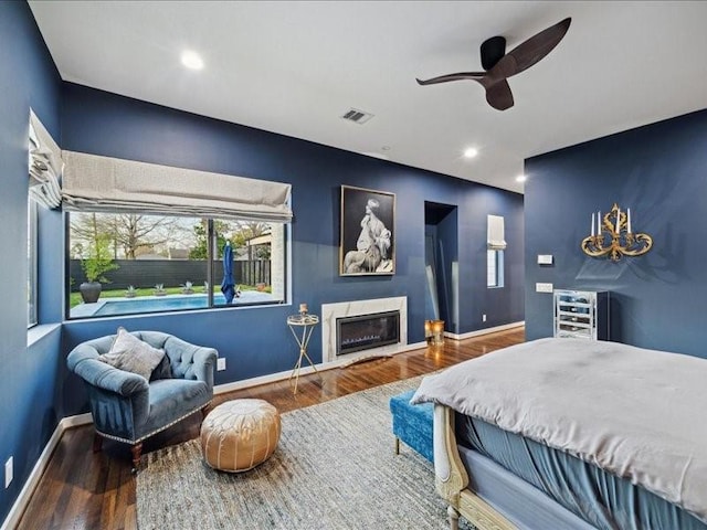 bedroom featuring a glass covered fireplace, wood finished floors, visible vents, and baseboards