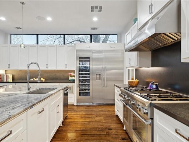 kitchen featuring under cabinet range hood, a sink, visible vents, white cabinets, and high end appliances