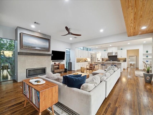 living area with a large fireplace, visible vents, dark wood-style flooring, and recessed lighting