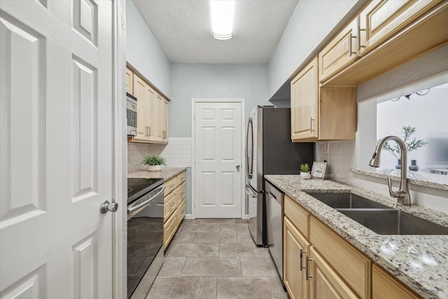 kitchen with appliances with stainless steel finishes, light brown cabinets, a sink, and light stone counters