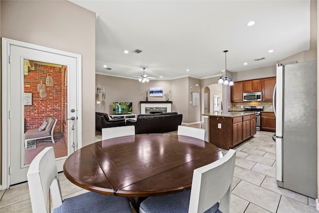 dining space featuring arched walkways, crown molding, a fireplace, light tile patterned floors, and a ceiling fan