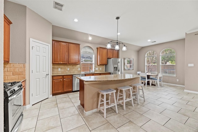 kitchen featuring visible vents, a breakfast bar area, a center island, light stone countertops, and stainless steel appliances