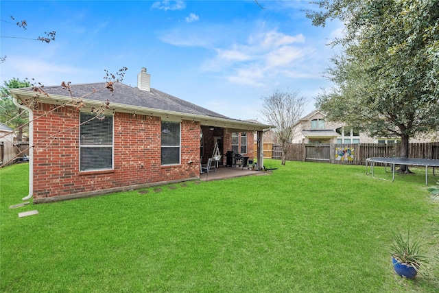 back of property with a trampoline, brick siding, a patio, a chimney, and a fenced backyard