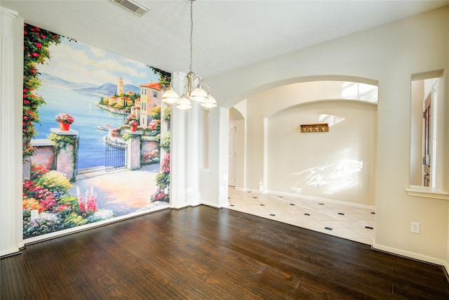 unfurnished dining area featuring arched walkways, a notable chandelier, visible vents, wood finished floors, and baseboards